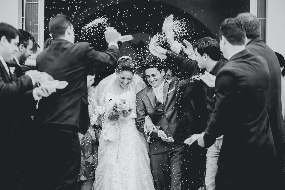 Black and white photo of bride and groom leaving church with rice being tossed