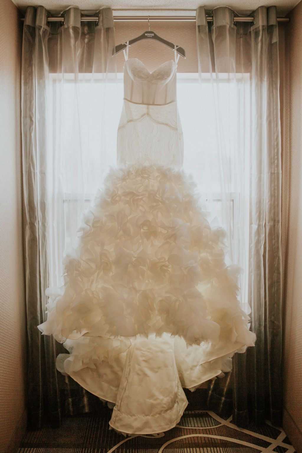 custom made Winnie Couture trumpet bridal gown hanging on display in window