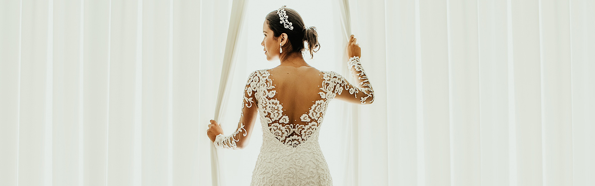 Gorgeous bride in long sleeved gown opening window