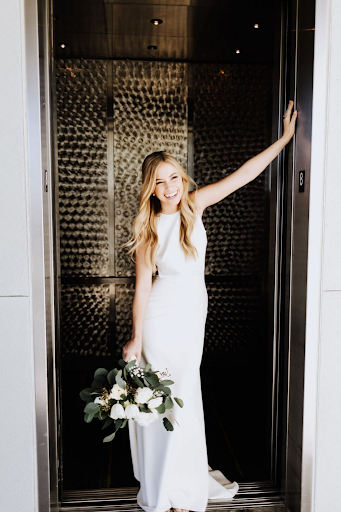Happy bride leaning in doorway in simple and elegant wedding dress