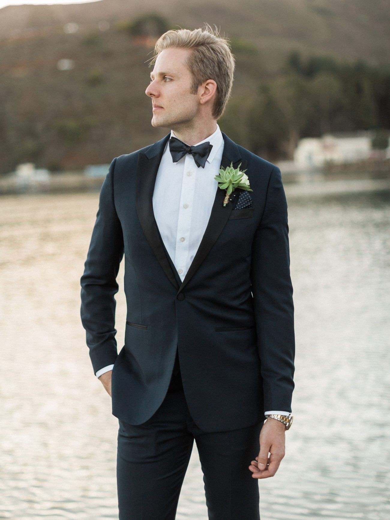 Groom wearing a suit and posing in front of a lake