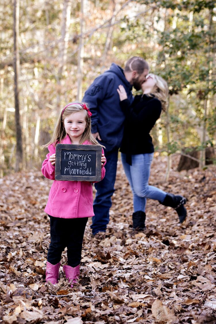 Little girl holding prop sign with couple in forest background