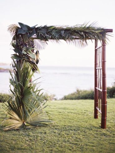 A tropical arch made from a simple bamboo frame and lush tropical palms is our favorite ceremony look. We love how the dark wood adds elegance and the monochromatic leaves help the focus shift on the texture of the foliage. We can imagine guests seated on dark-stained benches and the aisle lined with additional palm leaves.