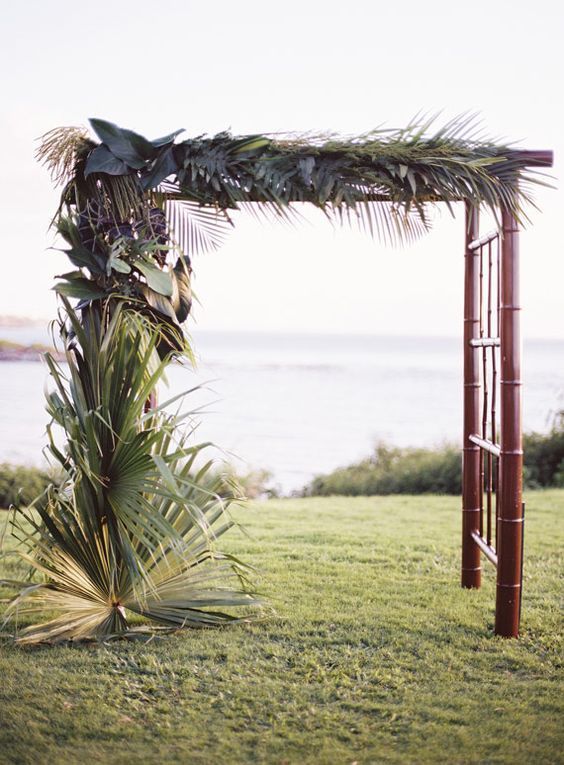 A tropical arch made from a simple bamboo frame and lush tropical palms is our favorite ceremony look. We love how the dark wood adds elegance and the monochromatic leaves help the focus shift on the texture of the foliage. We can imagine guests seated on dark-stained benches and the aisle lined with additional palm leaves.