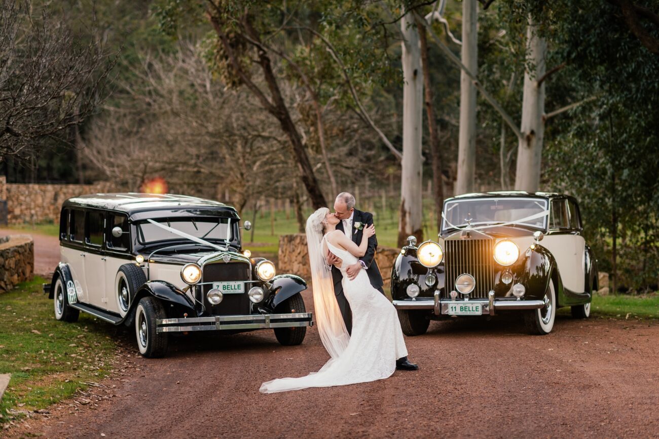 wedding couple standing in front of 2 vintage limos