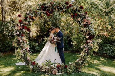 bride and groom standing next to outdoor flower arch