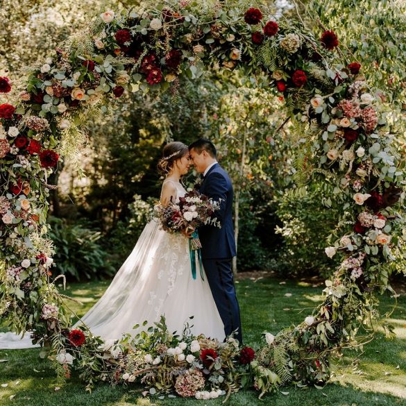 bride and groom standing next to outdoor flower arch